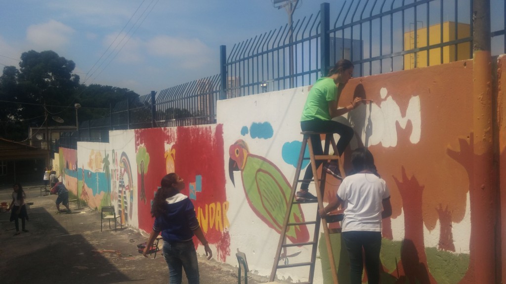 Alunos do projeto "Além dos muros da escola" pintando uma parede na cidade
